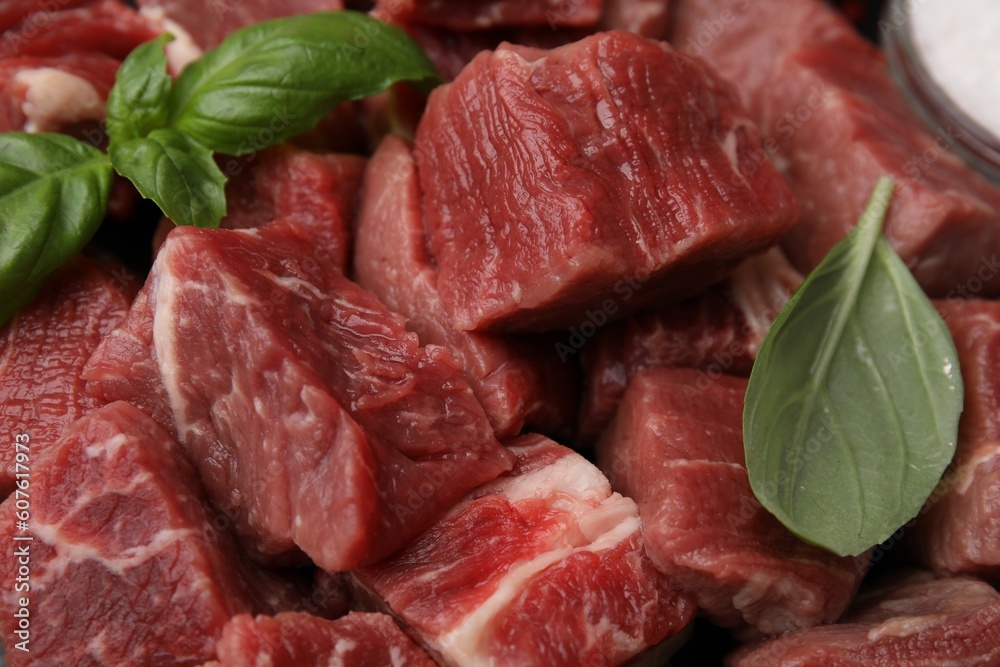 Cut fresh beef meat with basil leaves as background, closeup