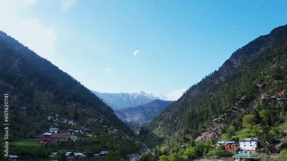 Beautiful view of the Himalayas snowy peaks in the background and a beautiful valley with a stream, forest, green fields, rooftops, and road of Kashmir Beautiful view of the Himalayas snowy peaks in the background and a beautiful valley with a stream, forest, green fields, rooftops, and road of Kashmir
