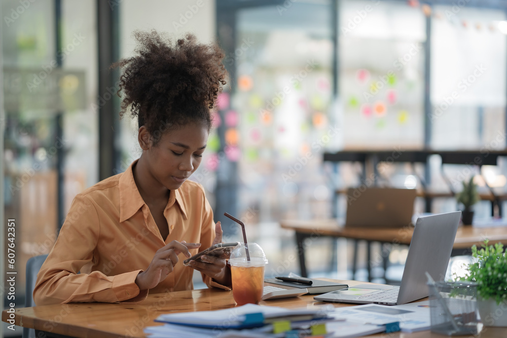 Focused young African female entrepreneur deep in thought while working at a table in a modern office. Focused young African female entrepreneur deep in thought while working at a table in a modern office.