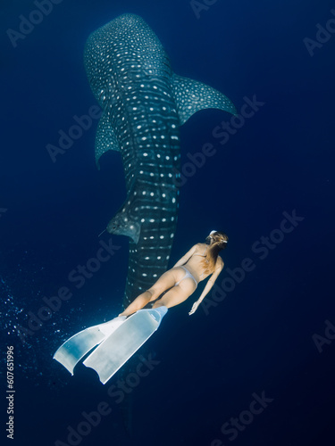 Young woman swim with Whale shark in deep blue ocean. Silhouette of giant shark swimming underwater and beautiful lady