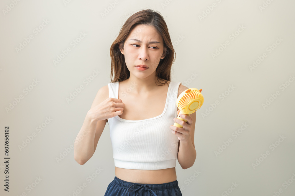 Suffering summer heat wave stroke, hot weather, tired asian young woman sweaty, refreshing with using portable fan hand, blowing wave fan to ventilation when temperature high, isolated on background. Suffering summer heat wave stroke, hot weather, tired asian young woman sweaty, refreshing with using portable fan hand, blowing wave fan to ventilation when temperature high, isolated on background.