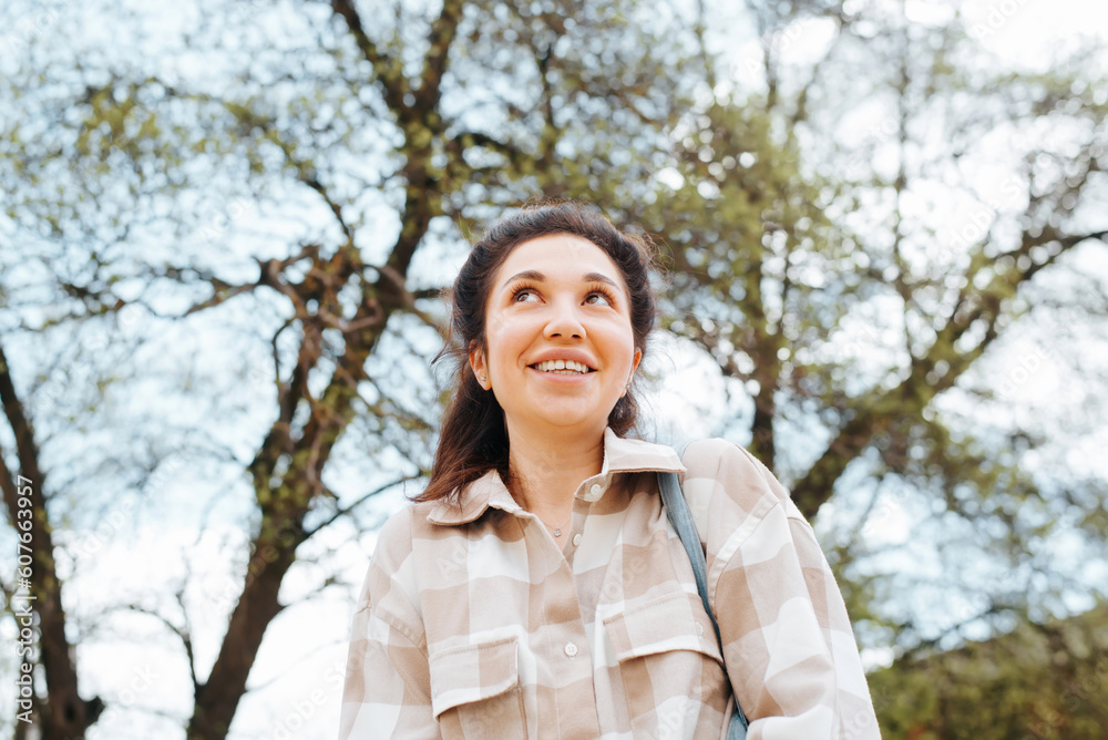 Portrait of pleased happy young mixed race woman in casual wear standing on tree and looking away, low angle view Portrait of pleased happy young mixed race woman in casual wear standing on tree and looking away, low angle view