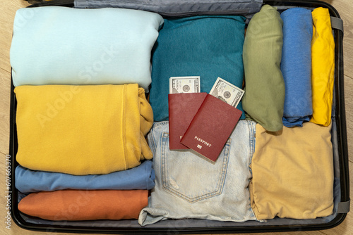 Top view of a suitcase with neatly stowed women's clothing, a passport and a stack of dollars. A couple of two women is preparing for a trip, air flight, resort vacation.