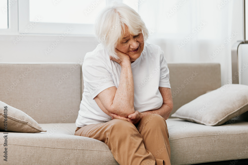 Elderly woman severe neck pain sitting on the sofa, health problems in old age, poor quality of life. Elderly woman severe neck pain sitting on the sofa, health problems in old age, poor quality of life.