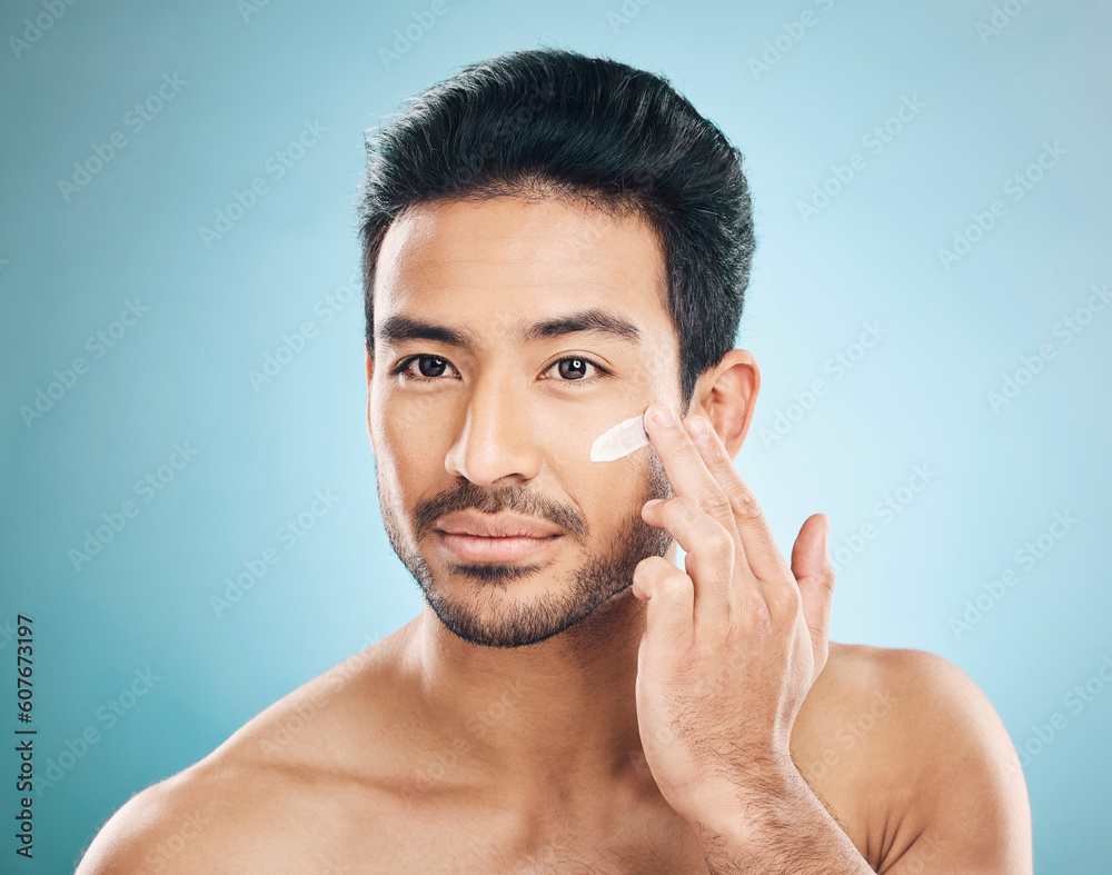 Obraz premium Wellness, skincare and man with face cream in a studio for a natural, moisturizing and health routine. Male model with facial spf, lotion or moisturizer for dermatology treatment by a blue background