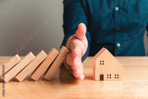 Home insurance and safety with hand protect house idea with people background. Hand covering wooden property and residence model from risk disaster and problem. After sales service representation. photo