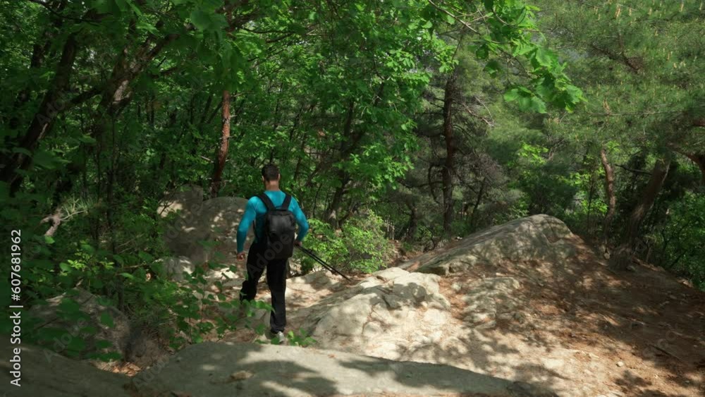Man Hiker Walking Way Down or Downhill on Steep Rocky Mountain Trail in Spring Green Trees Forest - High Angle Following Man Hiker Walking Way Down or Downhill on Steep Rocky Mountain Trail in Spring Green Trees Forest - High Angle Following
