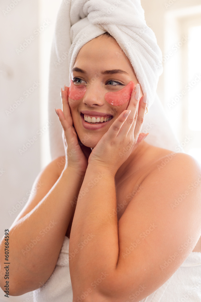 Closeup of plus size caucasian young woman wrapped with towels applying red eye patch in bathroom Closeup of plus size caucasian young woman wrapped with towels applying red eye patch in bathroom