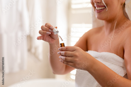 Midsection of plus size caucasian young woman wrapped in towel holding essential oil in bathroom photo