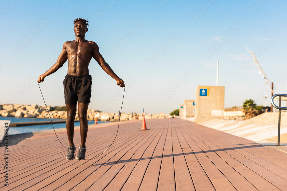 African man jumping rope on a beach. Young athlete man training outside.