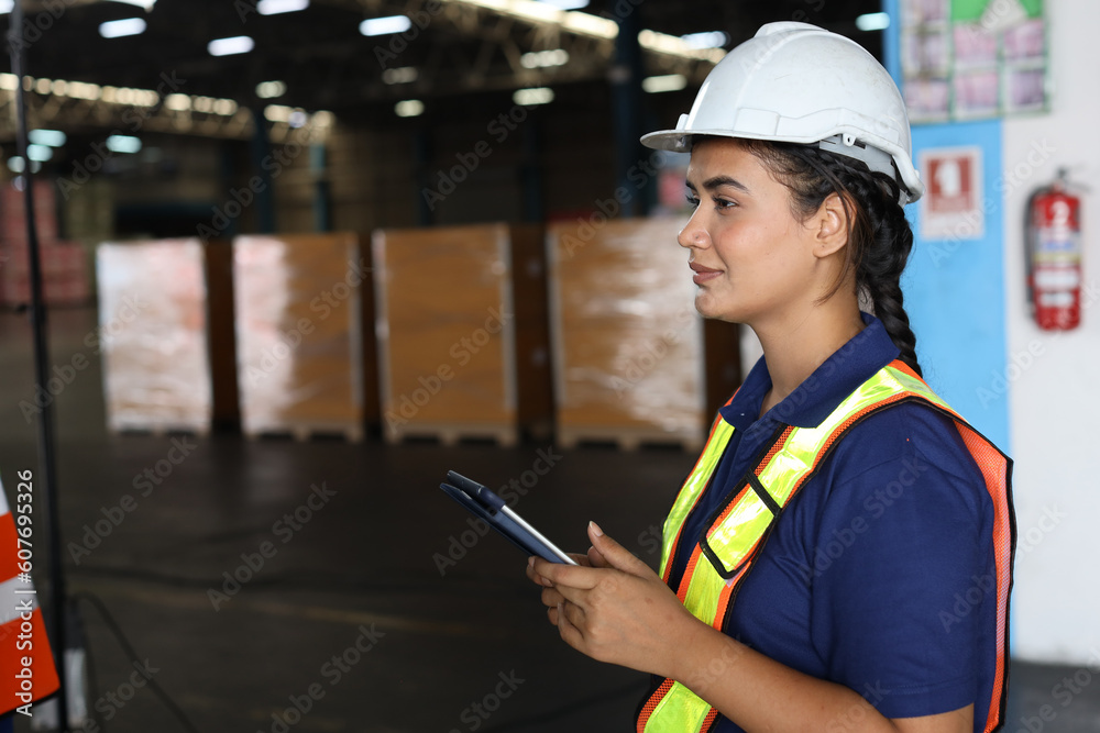 Fototapeta premium Warehouse workers woman with hardhats and reflective jackets using tablet, walkie talkie radio while looking away and controlling stock and inventory in retail warehouse logistics, distribution center