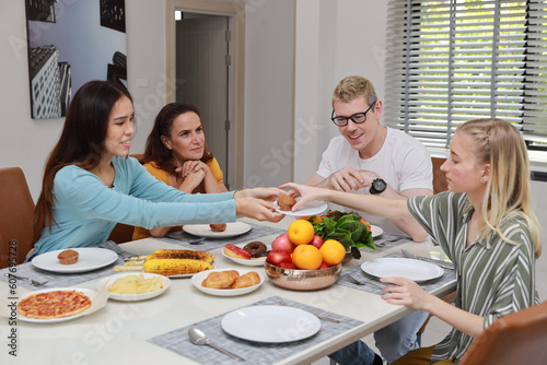 Group of happy diversity multiethnic family with different ages enjoy eating breakfast or dessert with salad, donuts and fruit in kitchen room at home. Happiness and healthy lifestyle concept.