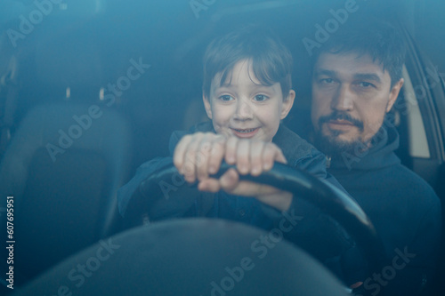 Smiling son learning to drive car with father seen through windshield photo
