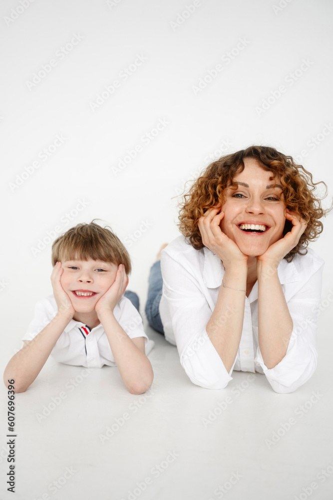 Happy woman lying down with son in front of white backdrop Happy woman lying down with son in front of white backdrop