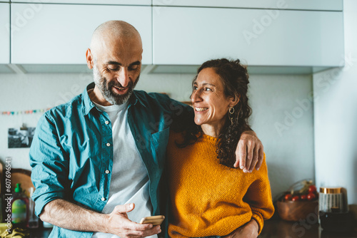 Man using smart phone by smiling woman in kitchen at home photo