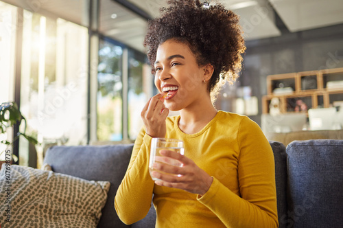 Glass, water and woman with medicine on sofa for health, self care and supplement at home. Relax, healthcare and happy african person with liquid drink and pill or tablet for wellness on couch photo