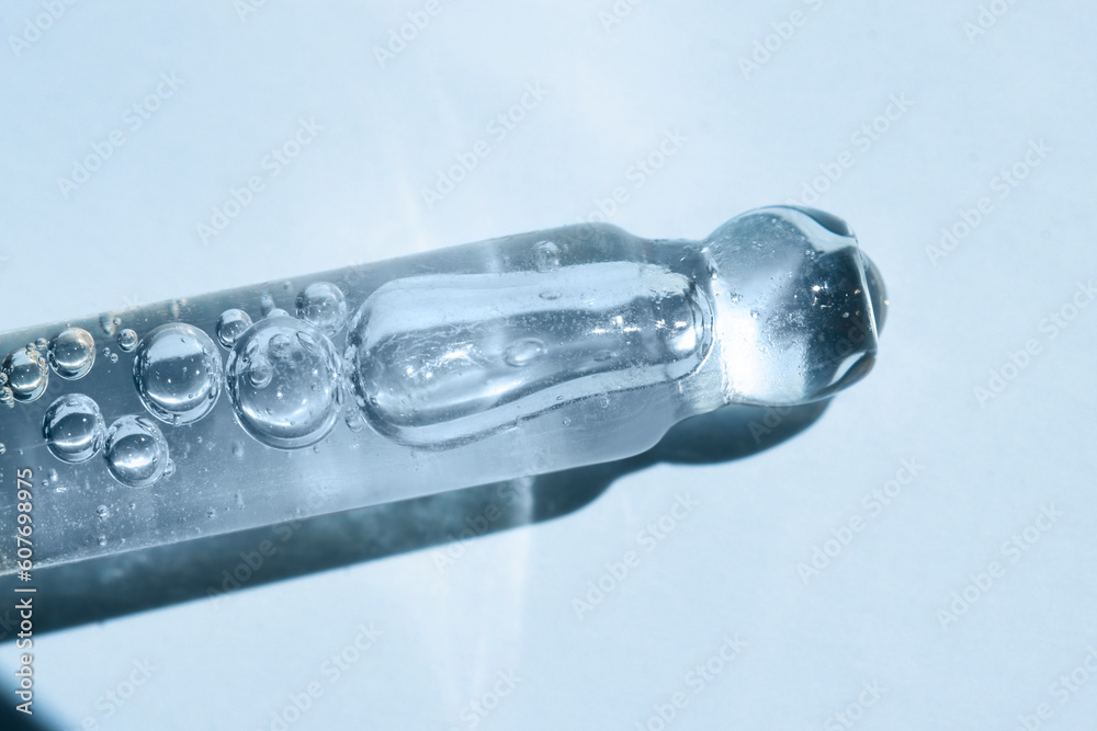 Glass dropper with transparent body serum, hyaluronic acid on a blue background, top view. Glass dropper with transparent body serum, hyaluronic acid on a blue background, top view.