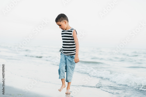 summer vacation at sea. Boy in striped T-shirt at seaside. Child running on beach having fun during summer holiday. happy kid playing at sunset time. Happy childhood. Travel and adventure concept #607698961