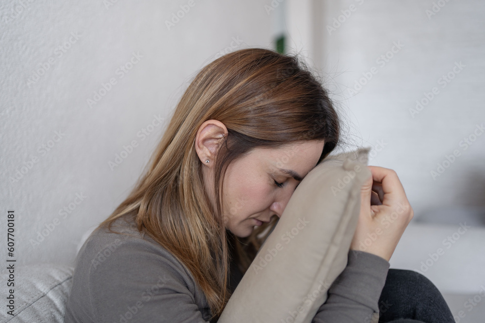 Young depressed woman sitting on sofa in living room. She feeling sad and worried suffering depression in mental health. Young depressed woman sitting on sofa in living room. She feeling sad and worried suffering depression in mental health.