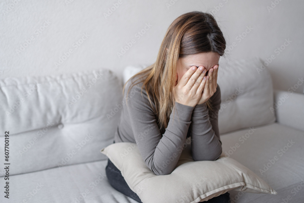 Young depressed woman sitting on sofa in living room. She feeling sad and worried suffering depression in mental health. Young depressed woman sitting on sofa in living room. She feeling sad and worried suffering depression in mental health.