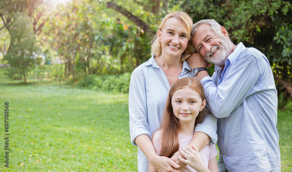 Fototapeta premium Portrait of happy family senior man woman and little girl relax in park. Mature elder family of three having fun together outdoor. Home school education, adopted child family lifestyle spring summer
