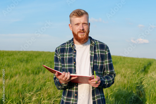 Portrait of an agronomist with a notebook in a wheat field. A farmer with a beard and a shirt prepares the field for the future harvest