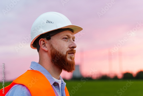 Portrait of a man in a white protective helmet and a reflective orange vest. Professional engineer. Beautiful sunset