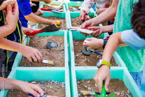 Children working as a archaeologists with brushes and shovels in containers with sand and stones, educations concept