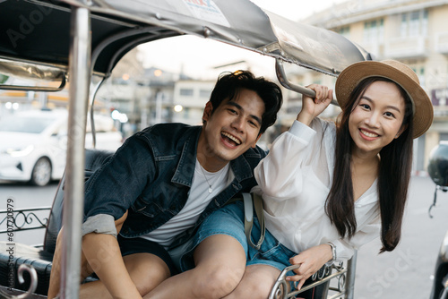 Happy and joyful Young Asian couple traveler tourists riding a tuk tuk tour, rickshaw style transportation on the street in Bangkok in Thailand - people traveling enjoying local culture concept