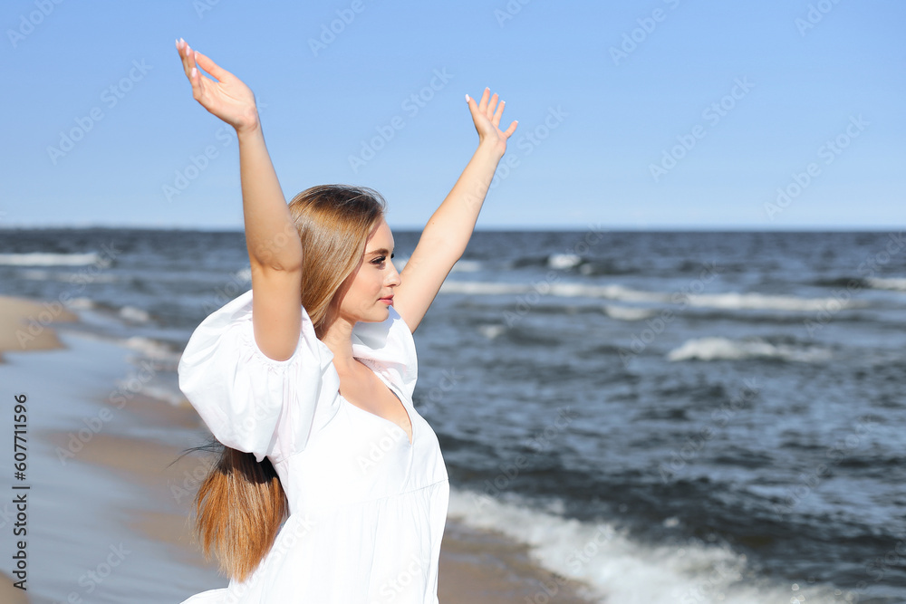 Happy, beautiful woman on the ocean beach standing in a white summer dress, raising hands. Happy, beautiful woman on the ocean beach standing in a white summer dress, raising hands.