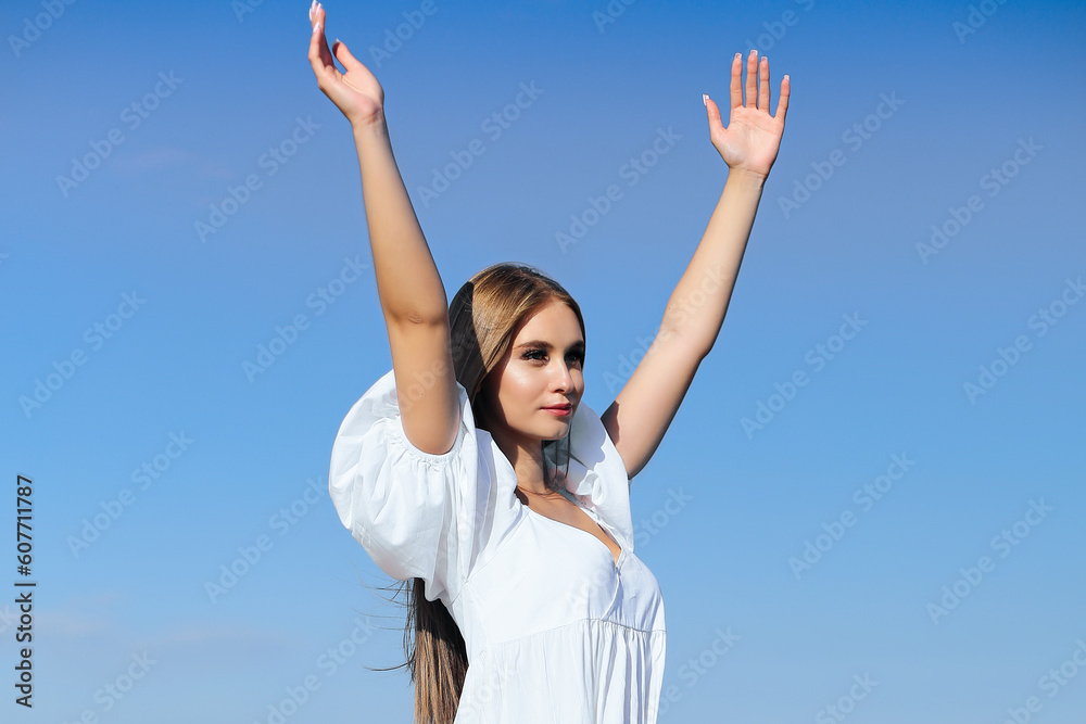 Happy, beautiful woman on the ocean beach standing in a white summer dress, raising hands. Happy, beautiful woman on the ocean beach standing in a white summer dress, raising hands.