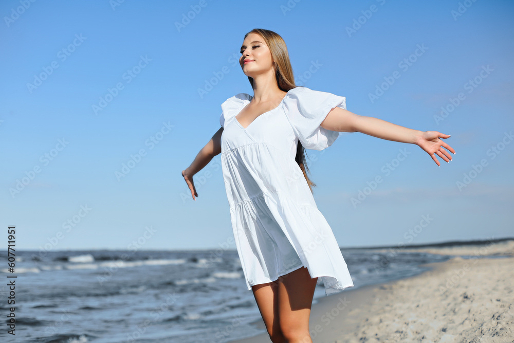 Happy smiling beautiful woman is on the ocean beach in a white summer dress, open arms. Happy smiling beautiful woman is on the ocean beach in a white summer dress, open arms.