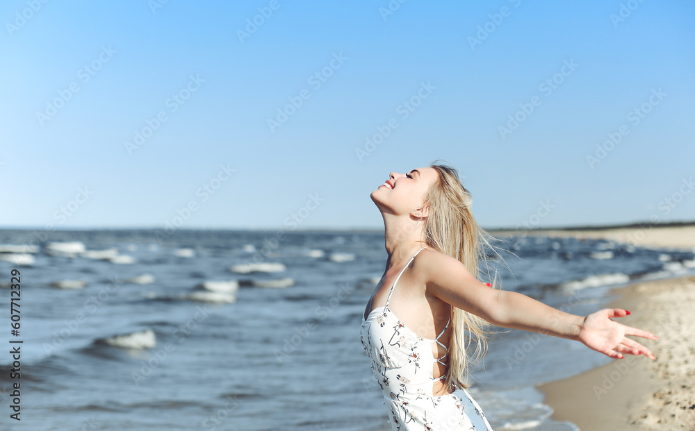 Happy blonde beautiful woman on the ocean beach standing in a white summer dress, raising hands. Happy blonde beautiful woman on the ocean beach standing in a white summer dress, raising hands.