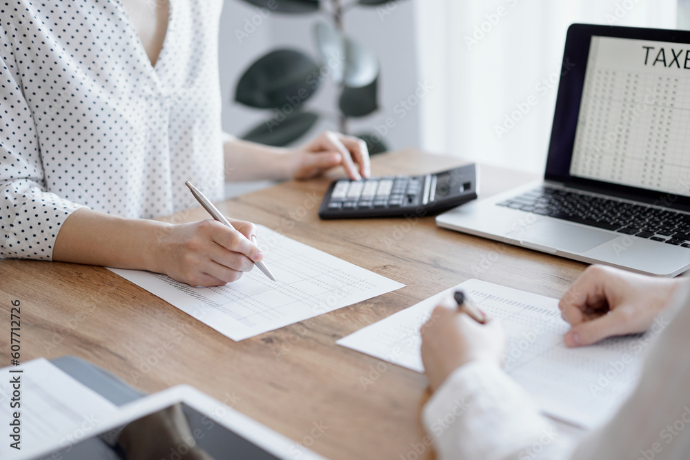 Woman accountant using a calculator and laptop computer while counting taxes with colleague at wooden desk in office. Teamwork in business audit and finance. Woman accountant using a calculator and laptop computer while counting taxes with colleague at wooden desk in office. Teamwork in business audit and finance.