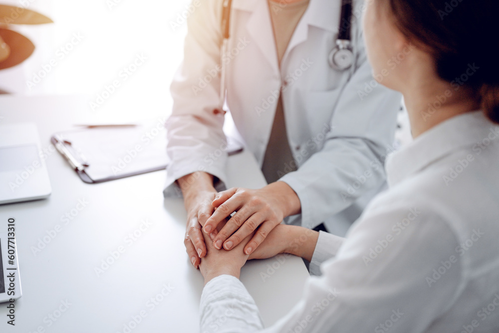 Doctor and patient sitting at the desk in clinic office. The focus is on female physician's hands reassuring woman, close up. Perfect medical service, empathy, and medicine concept. Doctor and patient sitting at the desk in clinic office. The focus is on female physician's hands reassuring woman, close up. Perfect medical service, empathy, and medicine concept.