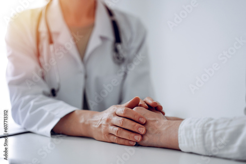 Doctor and patient sitting at the desk in clinic office. The focus is on female physician s hands reassuring woman  close up. Perfect medical service  empathy  and medicine concept.