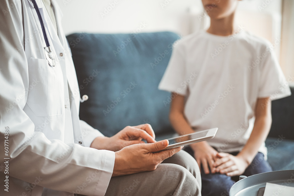 Obraz premium Doctor woman and kid boy patient at home. The pediatrician using tablet computer while filling up medical records, close up. Medicine, healthcare concepts.