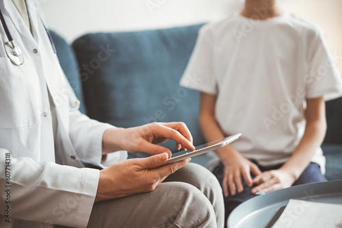 Doctor woman and kid boy patient at home. The pediatrician using tablet computer while filling up medical records, close up. Medicine, healthcare concepts.