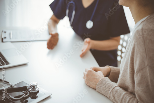 Doctor and patient sitting at the table in clinic while discussing something. The focus is on female patient's hands, close up. Medicine concept.