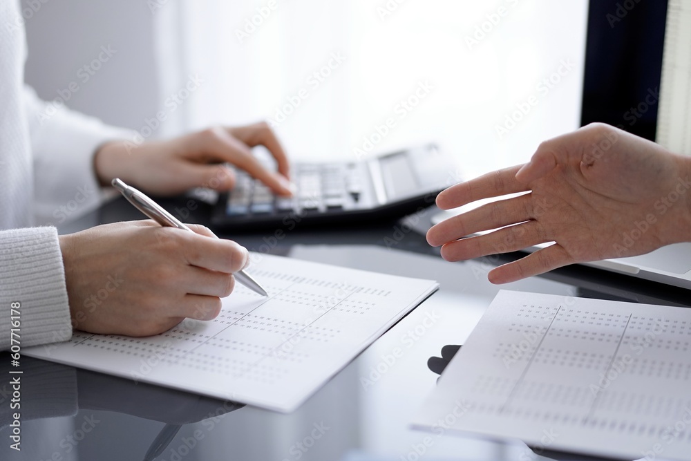 Woman accountant using a calculator and laptop computer while counting and discussing taxes with a client. Business audit concepts. Woman accountant using a calculator and laptop computer while counting and discussing taxes with a client. Business audit concepts.