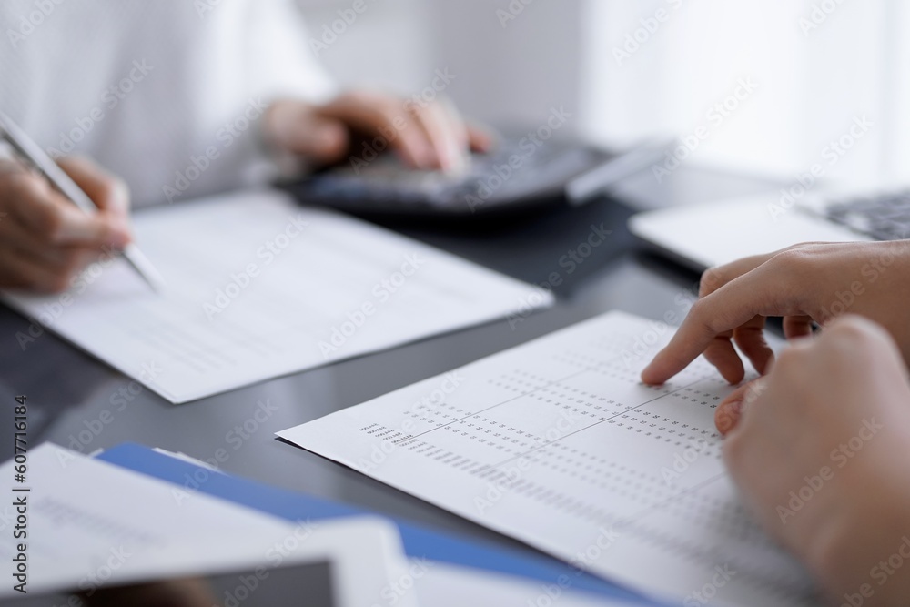 Woman accountant using a calculator and laptop computer while counting and discussing taxes with a client. Business audit concepts. Woman accountant using a calculator and laptop computer while counting and discussing taxes with a client. Business audit concepts.