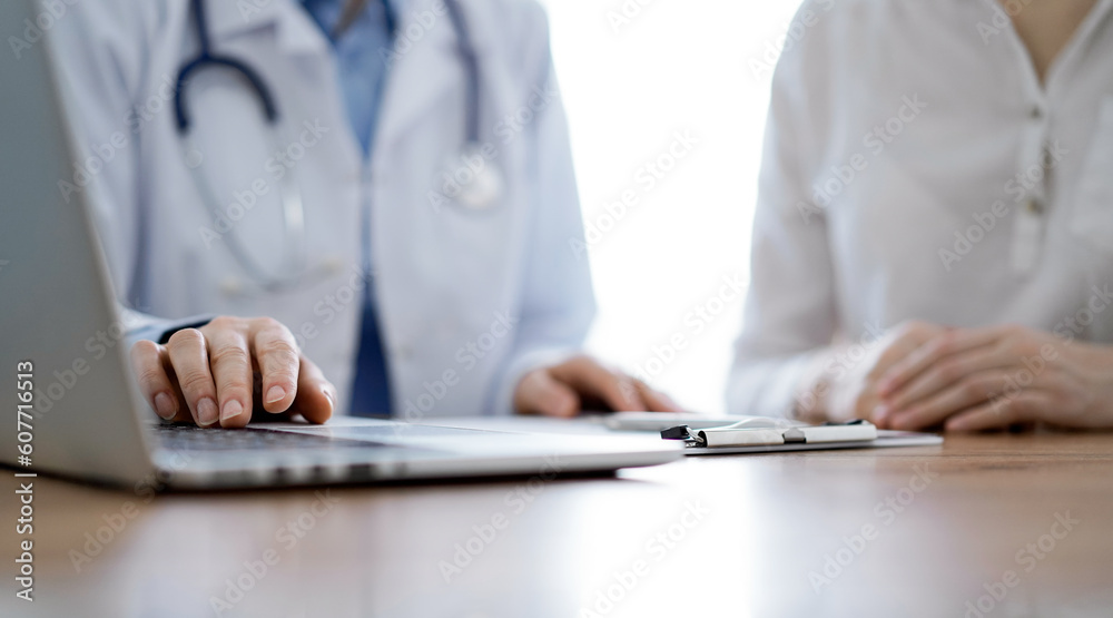 Doctor and patient discussing something while using laptop computer and sitting near each other at the wooden desk in clinic. Medicine concept. Doctor and patient discussing something while using laptop computer and sitting near each other at the wooden desk in clinic. Medicine concept.