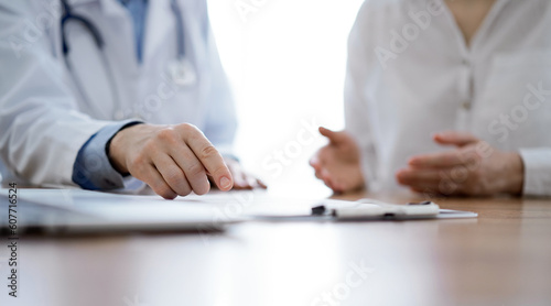 Doctor and patient sitting near each other at the wooden desk in clinic. Female physician s pointing to a records form. Medicine concept.
