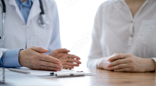 Doctor and patient discussing something while sitting near each other at the wooden desk in clinic  close up of hands. Medicine concept.