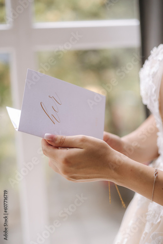 Close-up of bride hold vow in hands in front of big window at home. Preparing for wedding ceremony photo