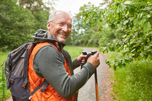 Happy elderly man holding poles hiking in forest photo