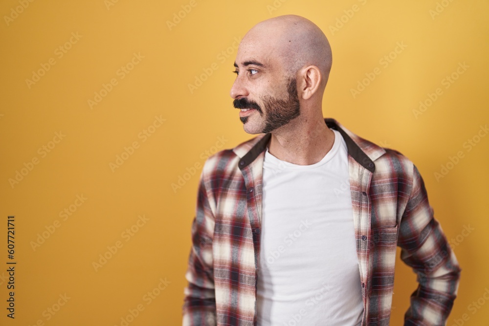 Hispanic man with beard standing over yellow background looking away to side with smile on face, natural expression. laughing confident.
