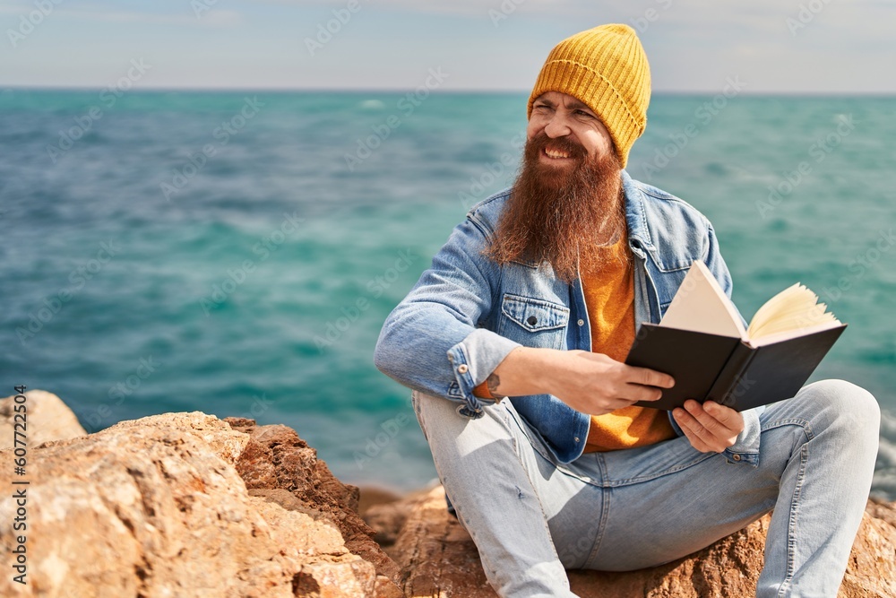 Young redhead man smiling confident reading book at seaside