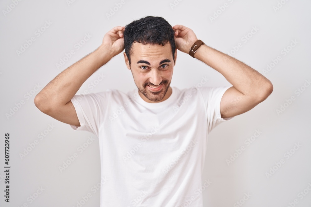 Handsome hispanic man standing over white background posing funny and crazy with fingers on head as bunny ears, smiling cheerful