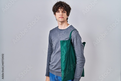 Obraz na plátně Young man wearing reusable bag thinking attitude and sober expression looking se
